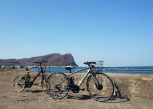 青い空と海、シリパ岬を背景に止まる2台の電動クロスバイクの写真