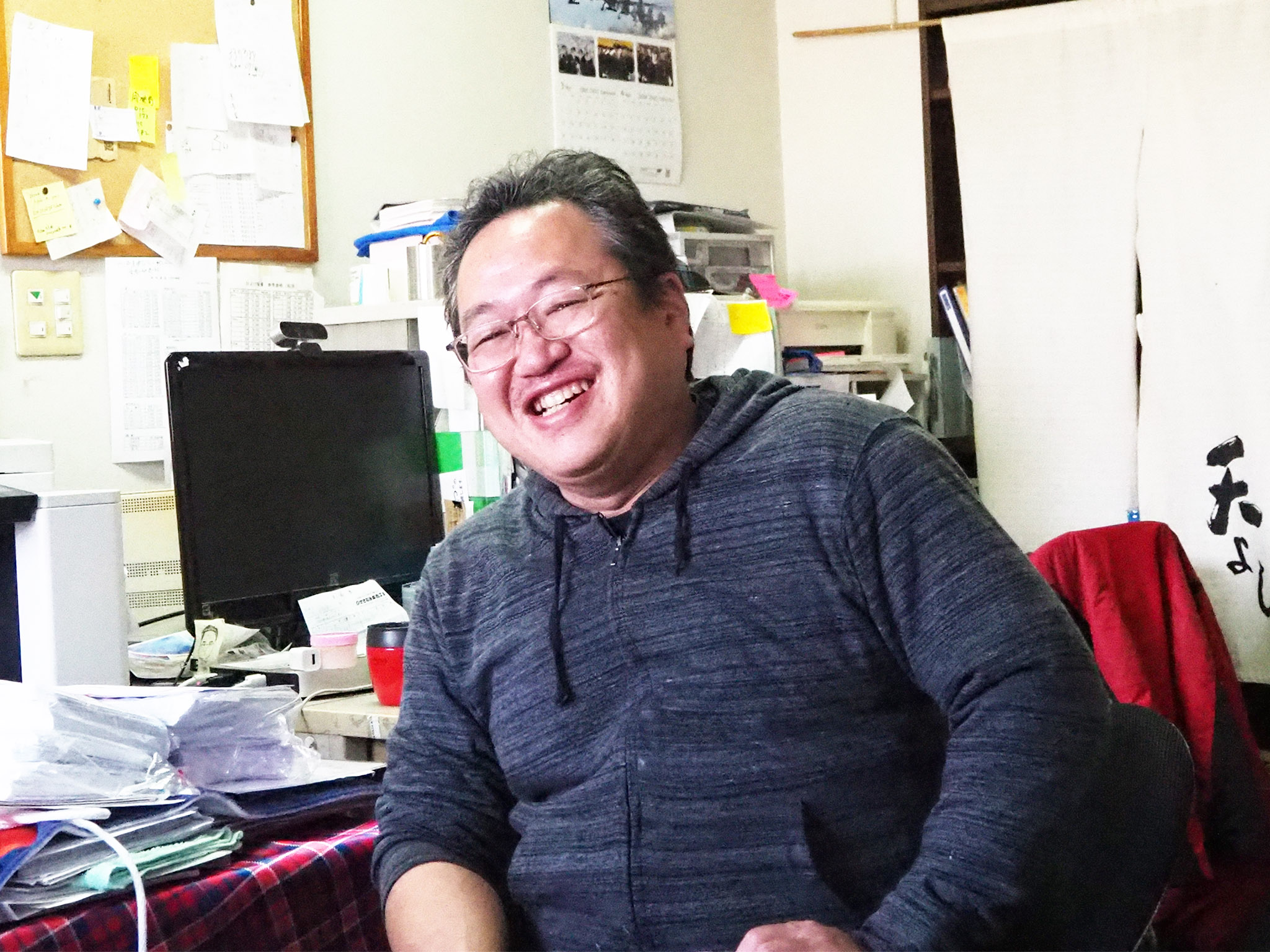 染色工房で座ってっ微笑む笹浪淳司さんの写真
